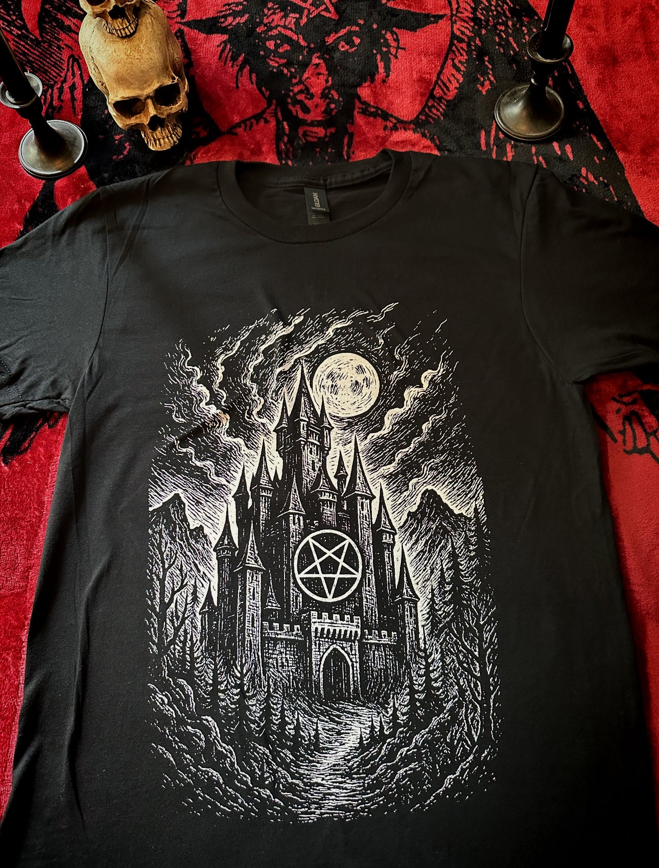 Tee features a white graphic of a gothic style castle with an inverted pentagram below a moon in a dark sky.