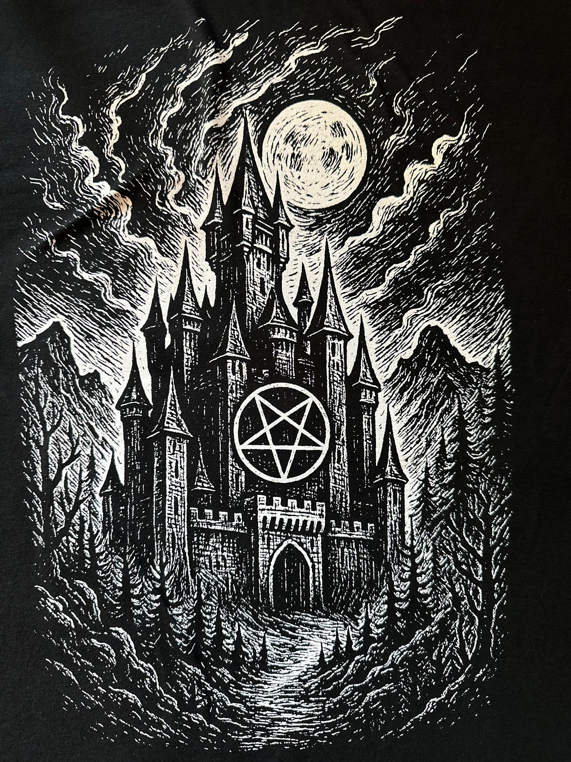 Tee features a white graphic of a gothic style castle with an inverted pentagram below a moon in a dark sky.